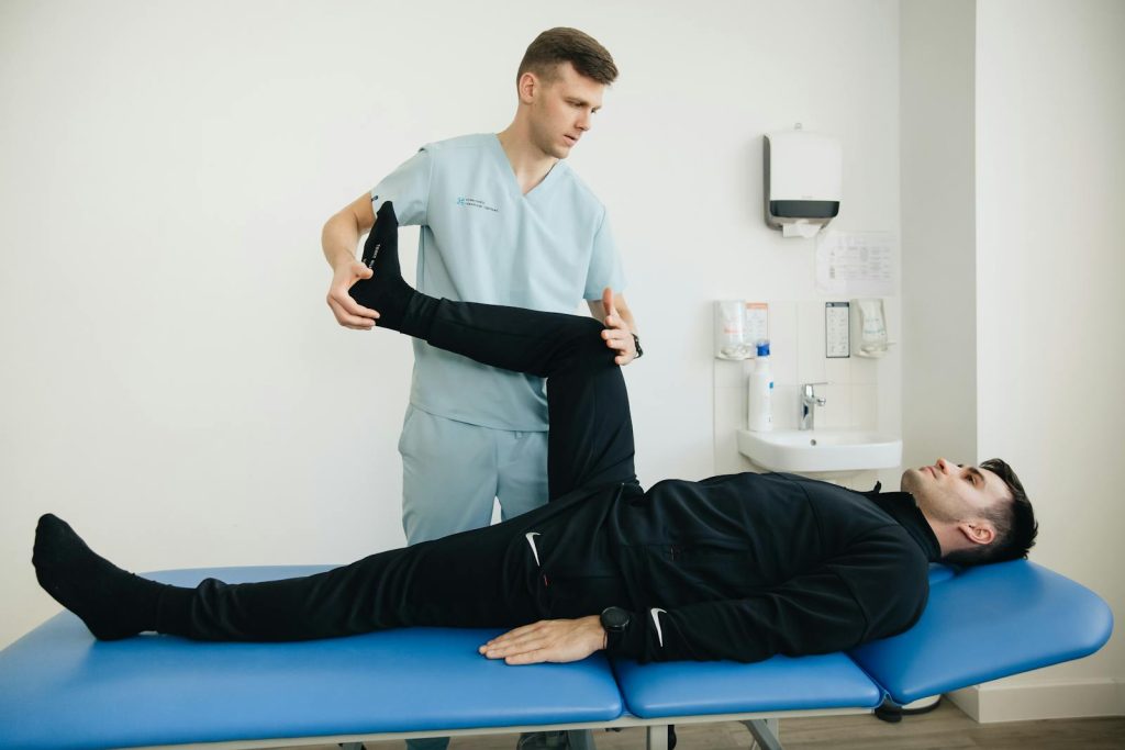 A physiotherapist assists a patient with leg stretching exercises on a treatment table.