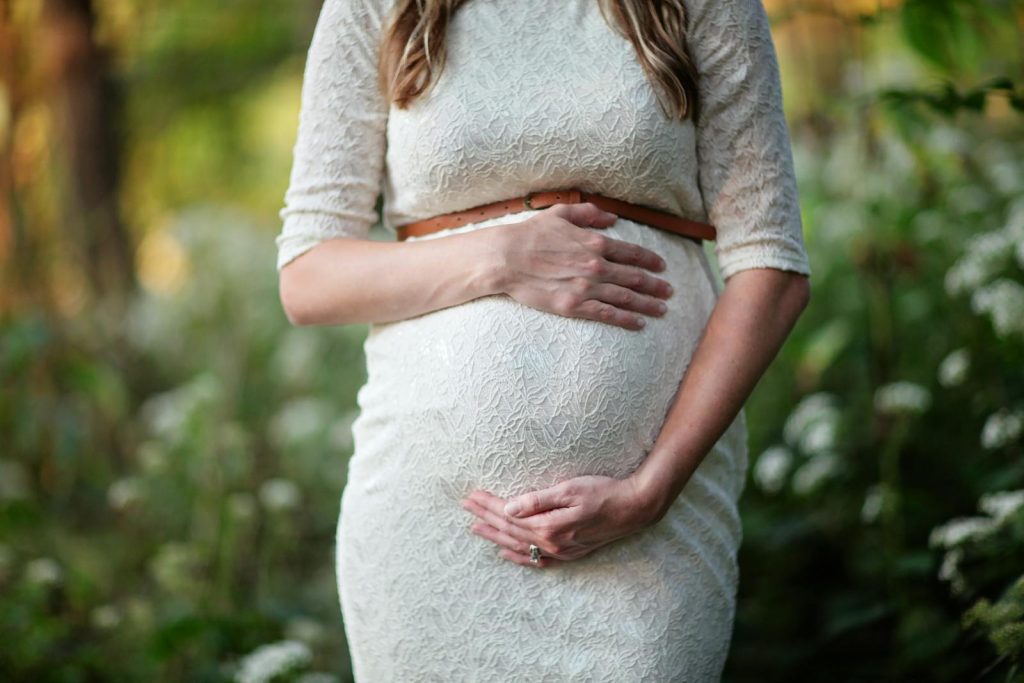 A pregnant woman in a lace dress gently cradling her belly in an outdoor setting.