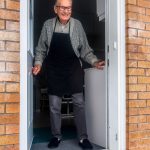 man in black vest and black dress pants standing beside white wooden door